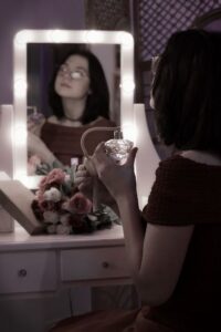 zdjęcie dziewczyny przed lustrem toaletki z perfumami w ręce 