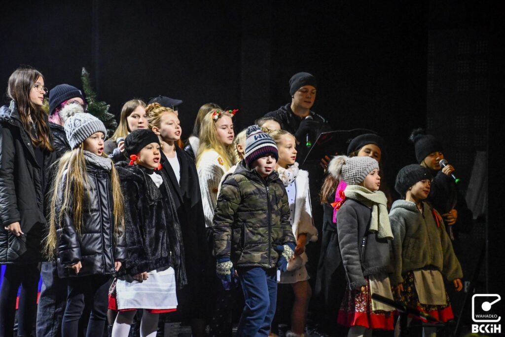 dzieci i młodzież śpiewają ubrani w zimowe kurtki i czapki 