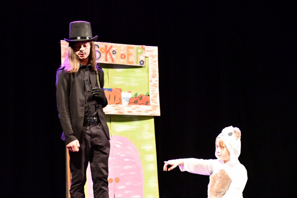 kard z przedstawienia dwoje dzieci w przebraniach teatralnych, w tle papierowa scenografia 